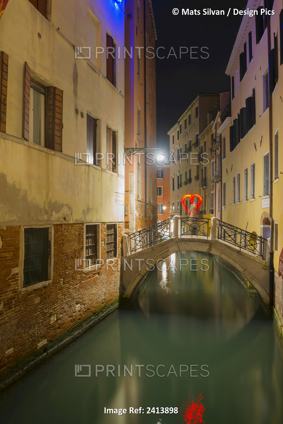 A Tranquil Canal Between Buildings With A Heart Shape On A Footbridge; Venice, ...