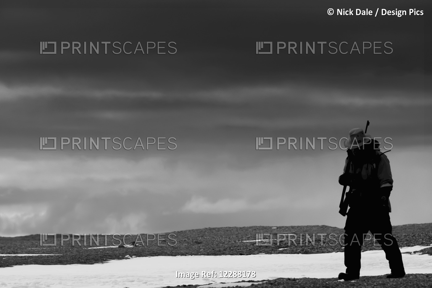A Black And White Image Of A Man Walking Over A Rocky Arctic Snowfield With A ...
