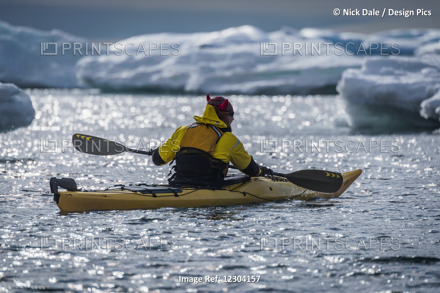 Backlit Kayaker Paddling By Icebergs In Sunlight; Antarctica