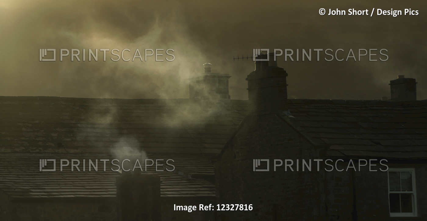 Smoke From Chimneys On A Rooftop Floats Into The Air; Reeth, Yorkshire, England