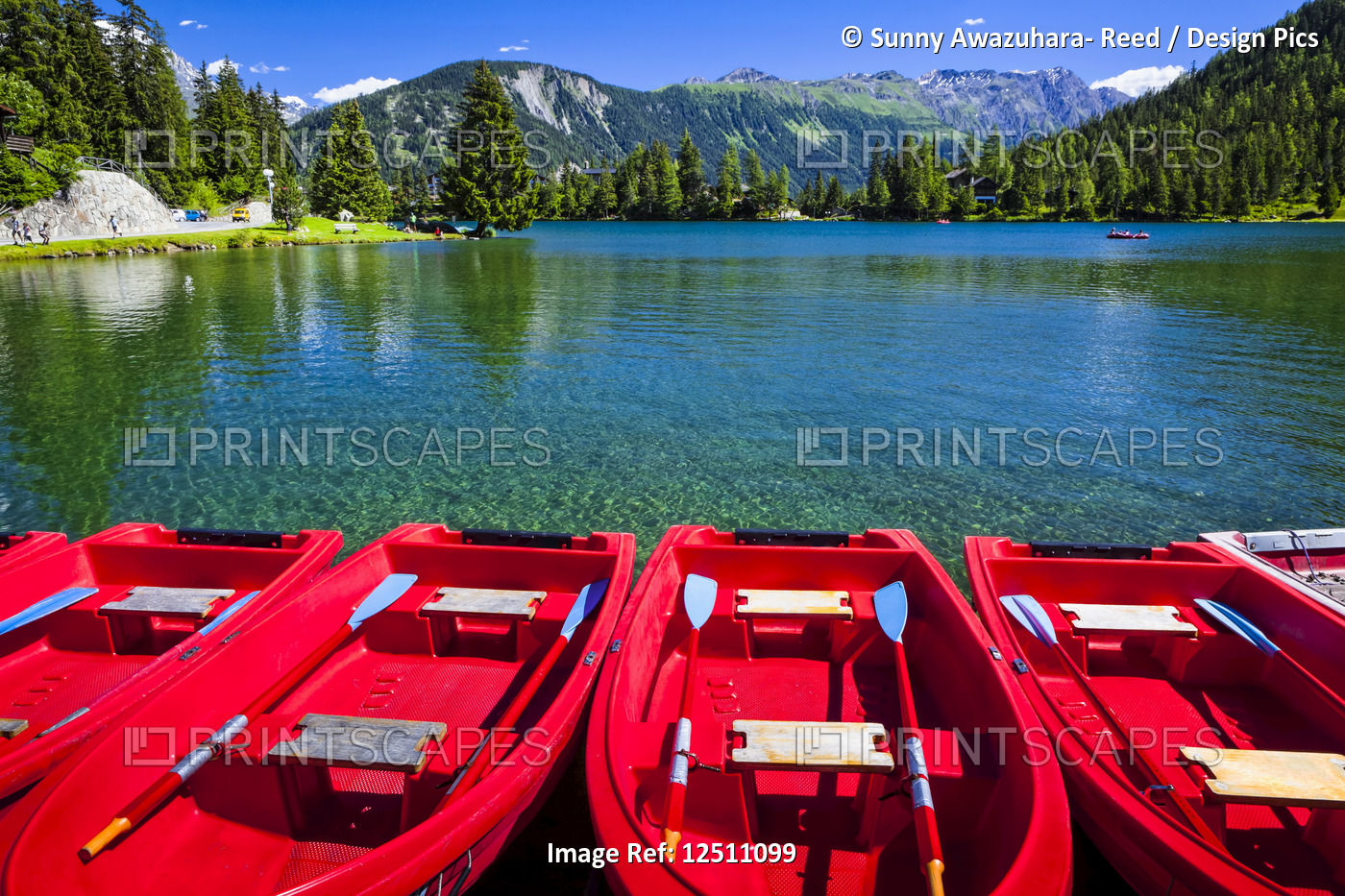 Red boats lined up at Champex Lake under blue sky with a mountain range in the ...