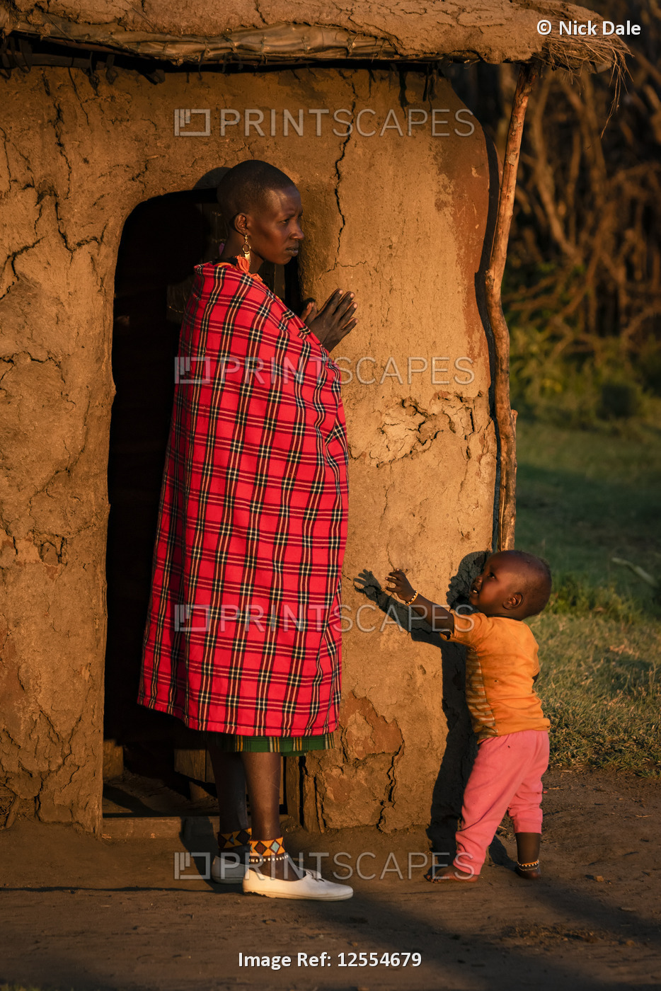 Woman in shuka with child outside hut; Tanzania