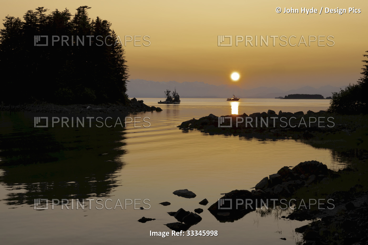 Silhouette of fishing trawlers along the rocky shoreline with the bright sun ...