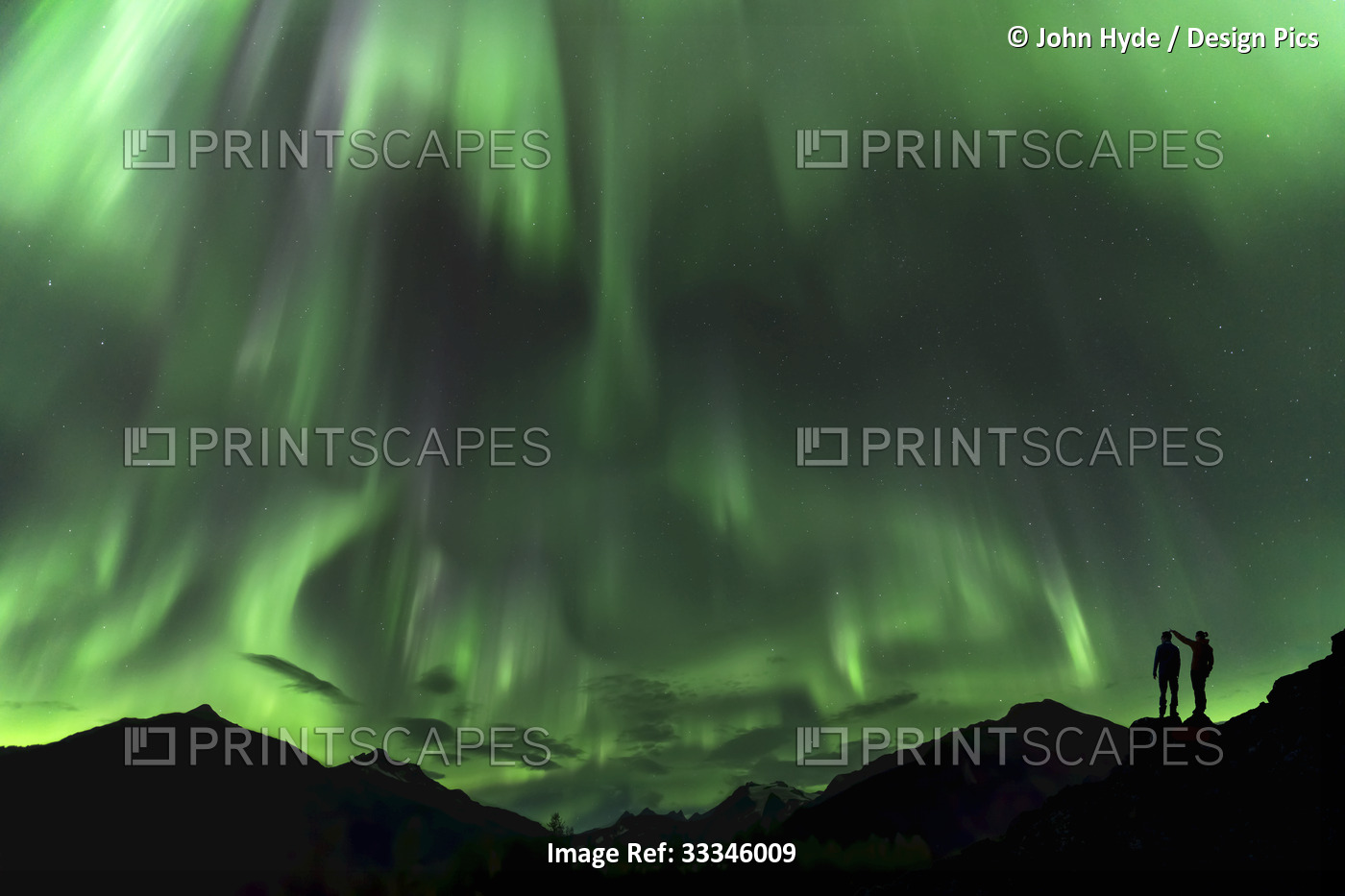 Silhouetted people and mountains with a green glowing Northern Lights display; ...