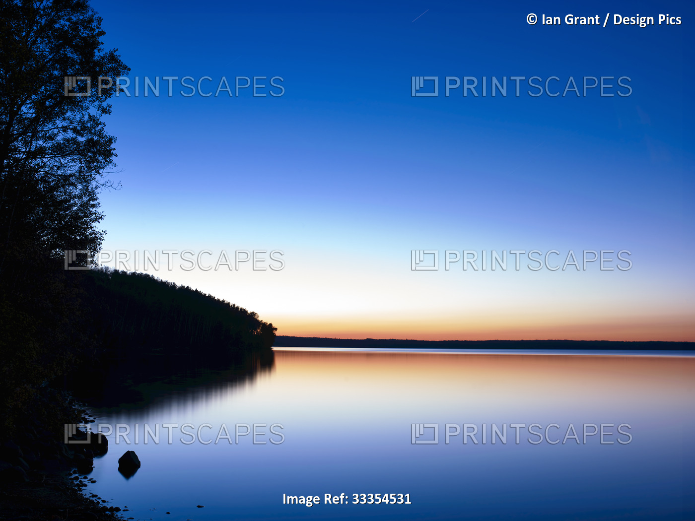 Glowing horizon at sunset reflected in tranquil water of Gregoire Lake; Fort ...